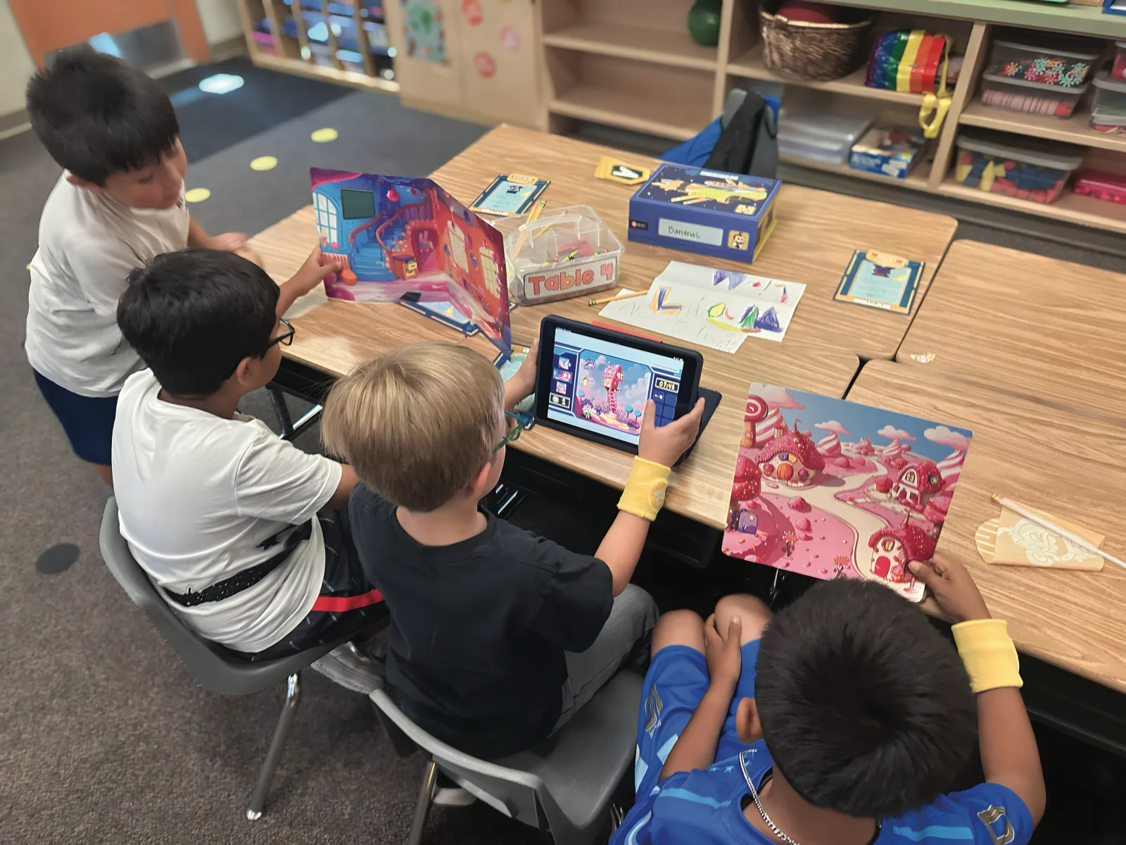 Young students gathered around pop-up scene boards and a tablet during a lesson